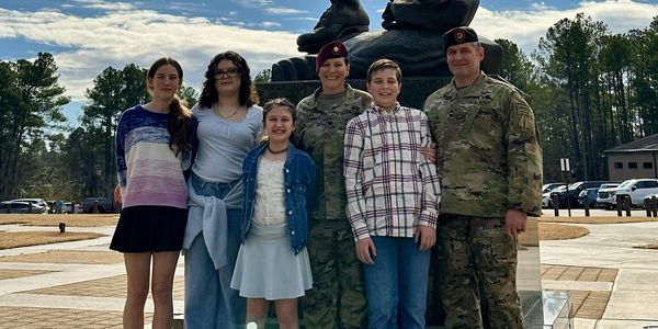 Family posing in front of a soldier statue on a sunny day.