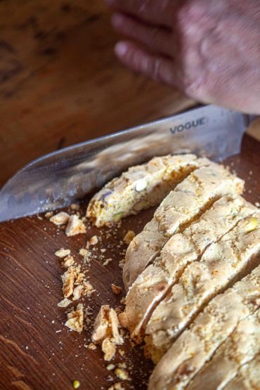 Hand slicing biscotti with a knife on wooden board.