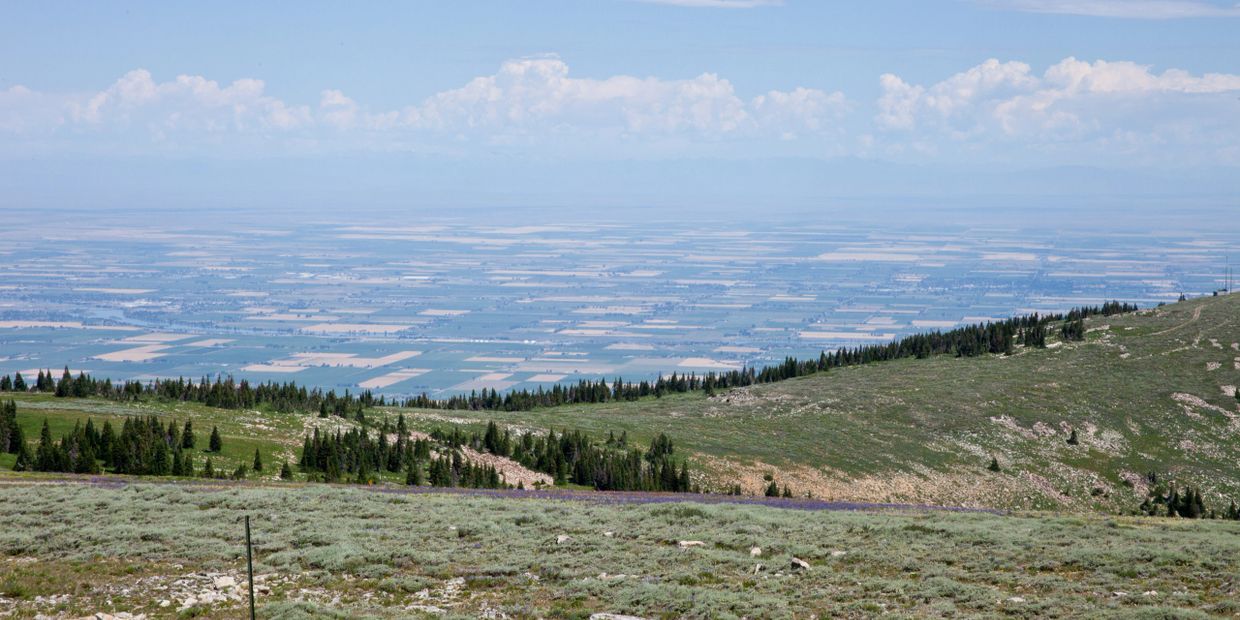Panoramic view of farmland from a green hillside under a partly cloudy sky.