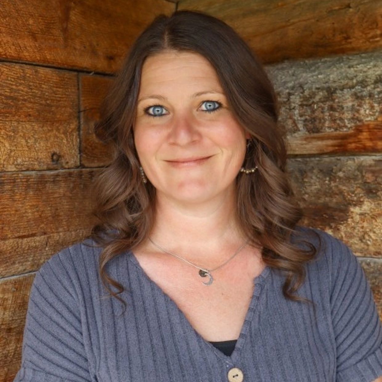 A woman with blue eyes smiles against a wooden wall background.