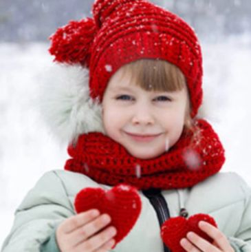Child in red knit hat and scarf holding red hearts in snow.