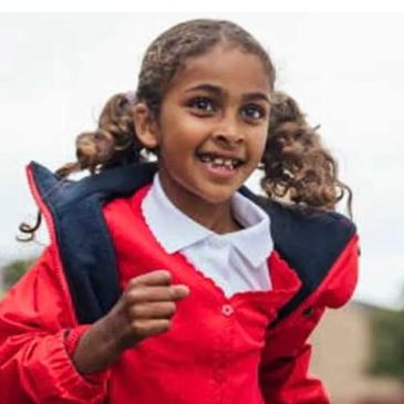 Happy young girl running outdoors in red jacket.