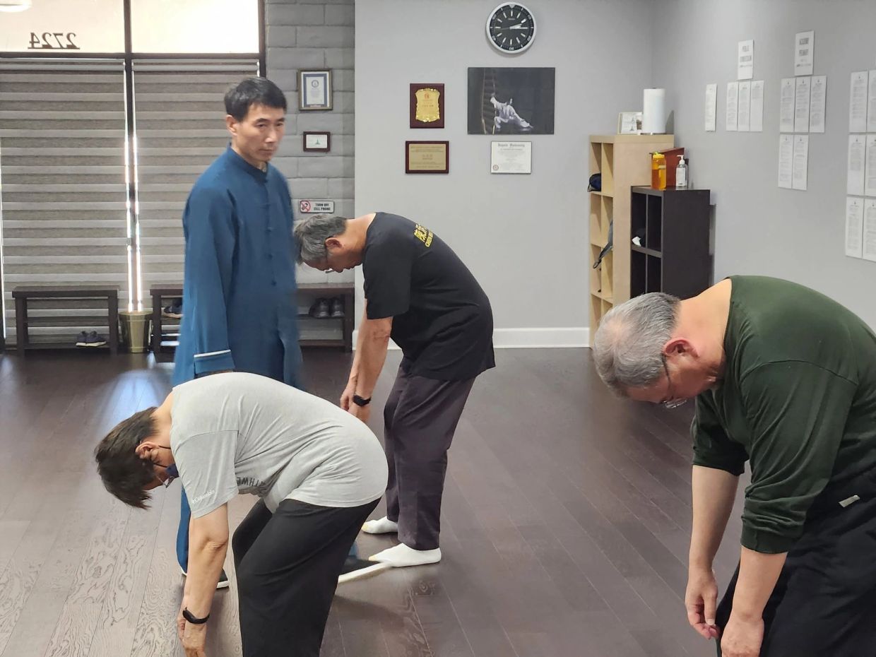 A martial arts instructor overseeing students stretching in a studio.