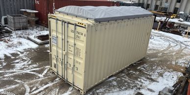 Beige shipping container with a covered top in a snowy yard.