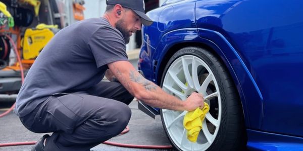 A man cleaning a white car wheel with a yellow cloth.