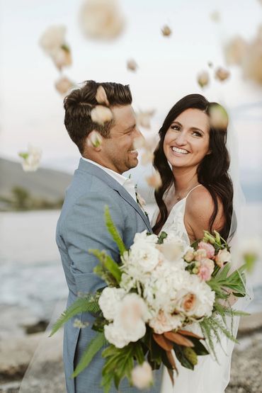 Bride holding bouquet and looking toward photographer as groom looks at his new wife