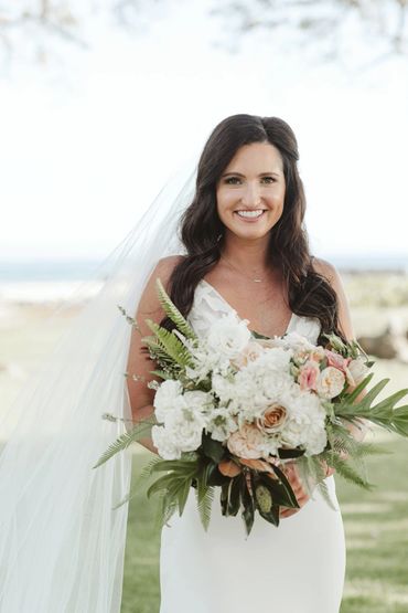 Bride holding beautiful bouquet of white flowers with a few pink flower accents 