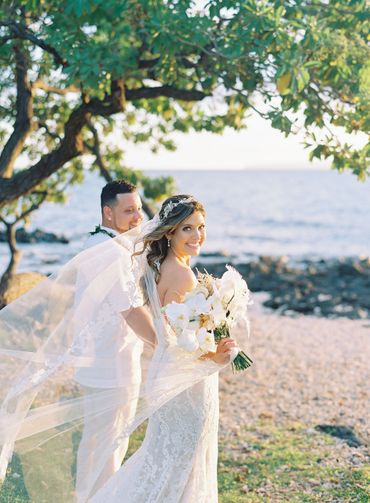 Bride and groom holding hands on the beach with bride looking back toward the camera