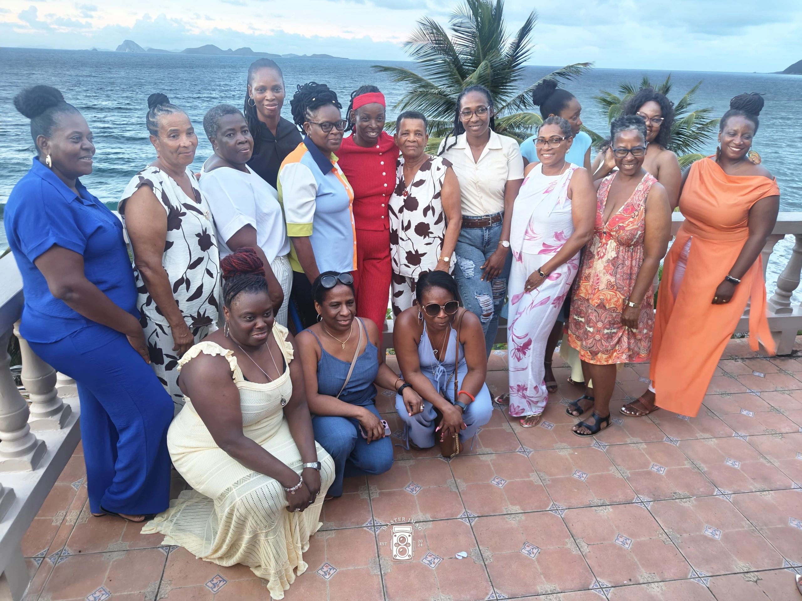 Group of women posing happily by the sea with palm trees in the background.