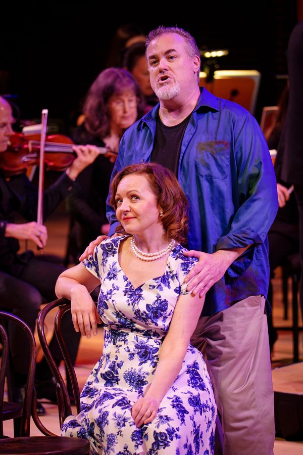 Actors perform a dramatic scene with live orchestra in the background.