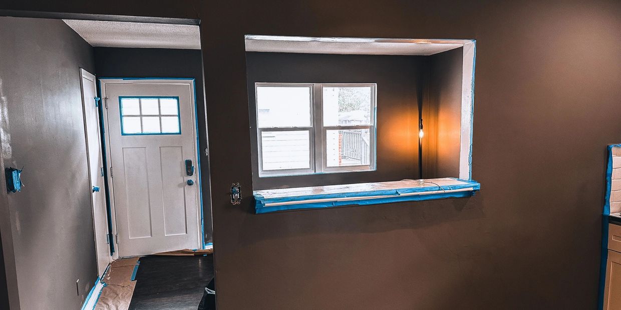 Room with brown walls, white door, and window under renovation with painter's tape.