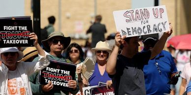 Protesters holding signs against Trump and for democracy at a rally.