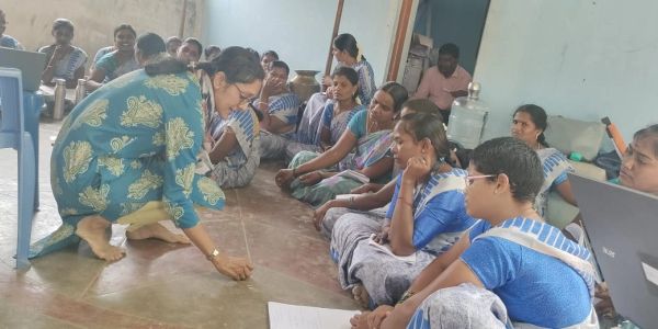 A woman leads a group sitting on the floor in a discussion or lesson.