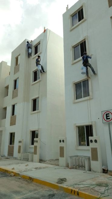 Workers painting the exterior of a multi-story building while suspended by ropes.