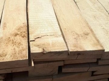 Stack of rough-cut wooden planks piled together.