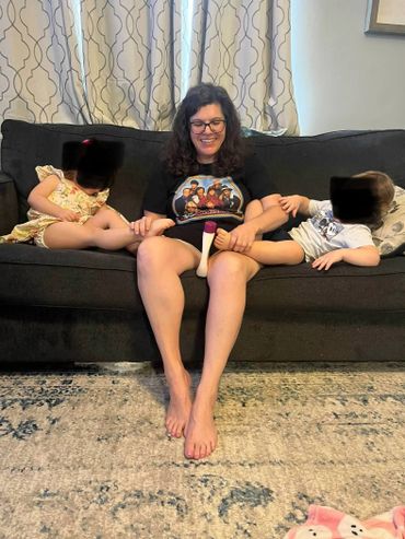A woman sitting on a couch with two children holding their feet, smiling.
