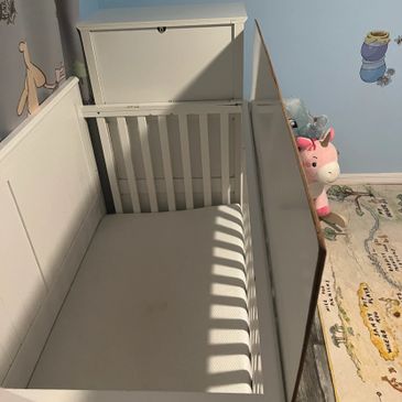 Empty white baby crib in a nursery with soft toys nearby.