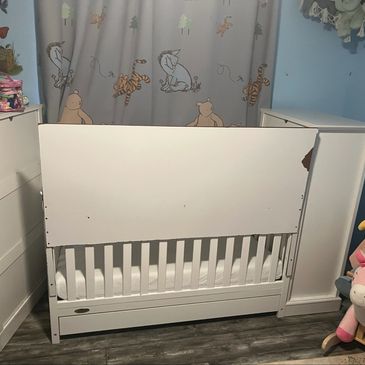 White baby crib in a nursery with Winnie the Pooh curtains.