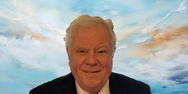 Elderly man smiling in front of a blue sky background.