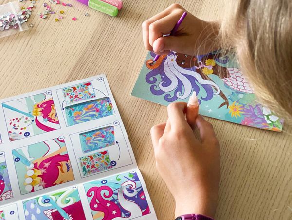 Child decorating a mermaid craft with sequins and glue.