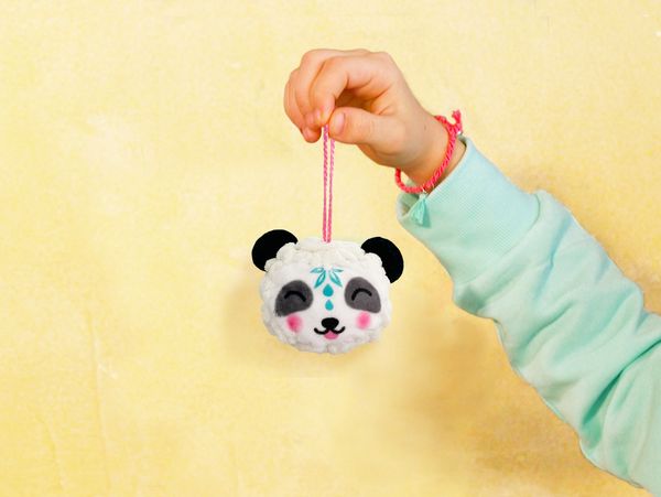 Hand holding a cute panda ornament with a pink string.