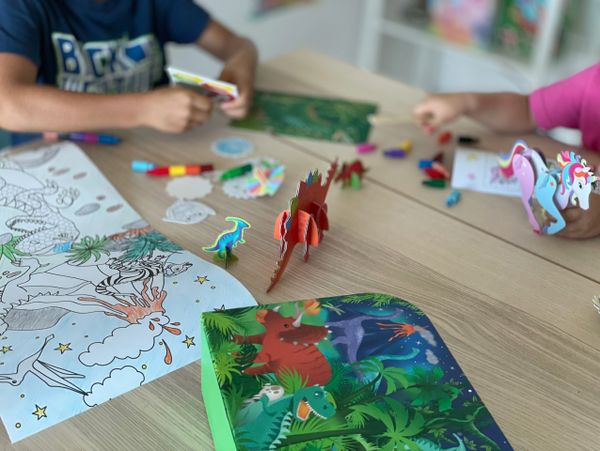 Children playing with dinosaur and unicorn toys around coloring sheets.