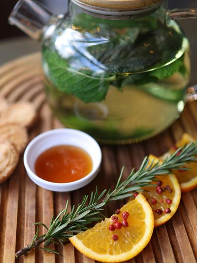 Herbal tea setup with fresh mint, orange slices, honey, and rosemary on a wooden tray.