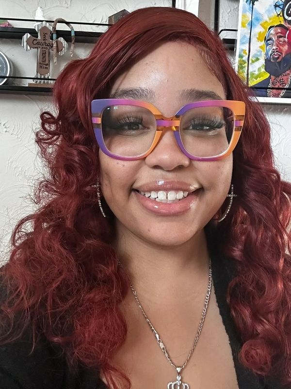 Woman with curly red hair wearing colorful glasses and a big smile.