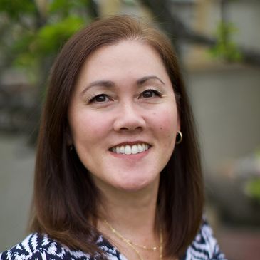 Smiling woman with brown hair outdoors, wearing a patterned top.