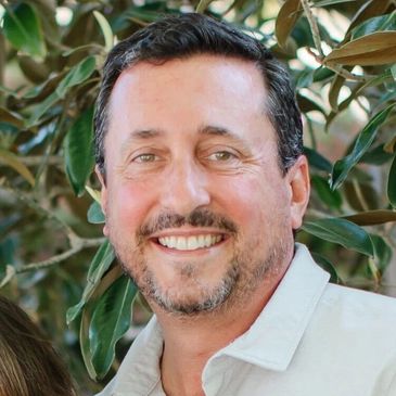 Smiling man with short dark hair and a trimmed beard outdoors.