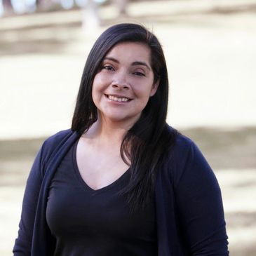 A smiling woman with long dark hair outdoors.
