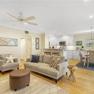 Cozy living room with beige sofa and open kitchen in the background.