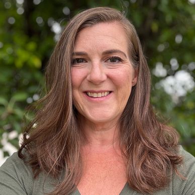 Smiling woman with long brown hair outdoors in natural setting.