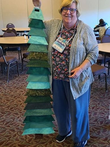 Woman proudly displays a handmade fabric Christmas tree decoration indoors.