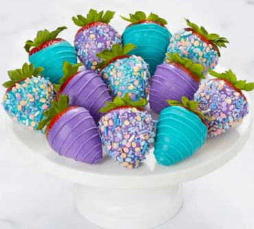 Colorful strawberries dipped in blue and purple chocolate with sprinkles on a white cake stand.