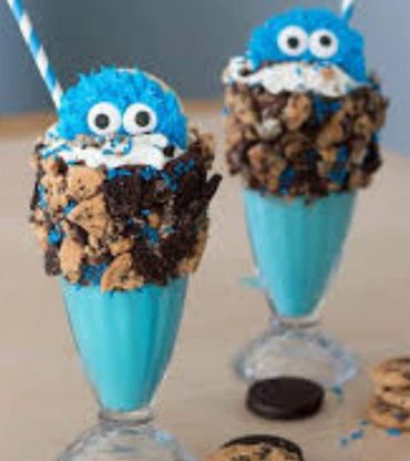 Two blue milkshakes decorated with Cookie Monster faces and cookie crumbles.