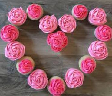 Cupcakes with pink frosting arranged in a heart shape on a wooden surface.