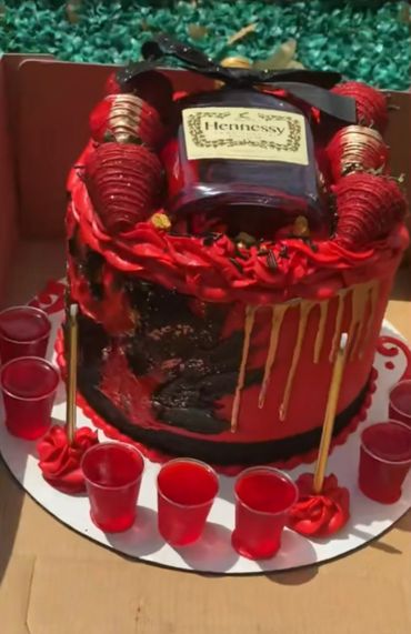 Red and black cake with Hennessy bottle and red shot glasses.