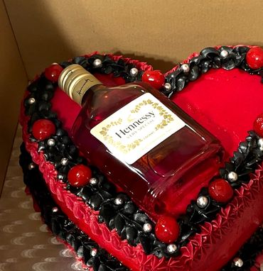Heart-shaped red cake with black and red decorations topped with a bottle of Hennessy.