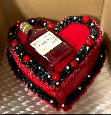 Heart-shaped red cake with black and red decorations topped with a bottle of Hennessy.