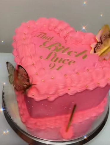 Heart-shaped pink cake with gold writing and butterfly decorations.
