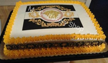 Rectangular cake with golden-yellow icing and ornate black and gold design on top.