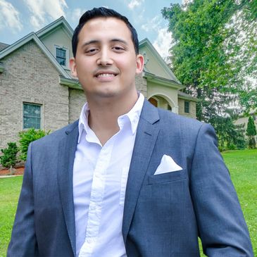 A man in a gray suit standing outdoors in front of a house.