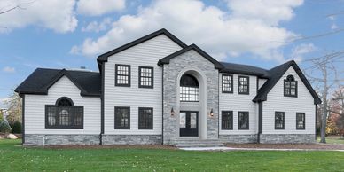 Modern two-story white house with stone accents and black window frames under a blue sky.