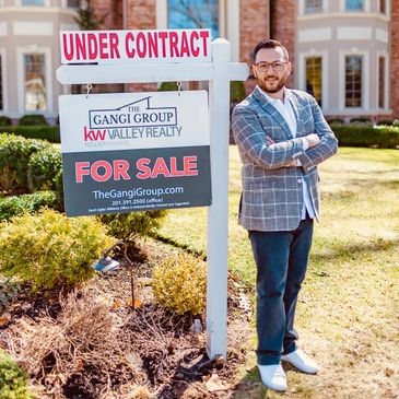 Real estate agent standing beside an under contract home sale sign.
