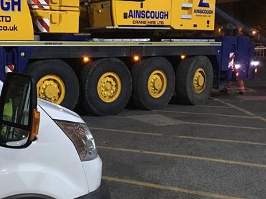A yellow crane truck and a white van parked at night.