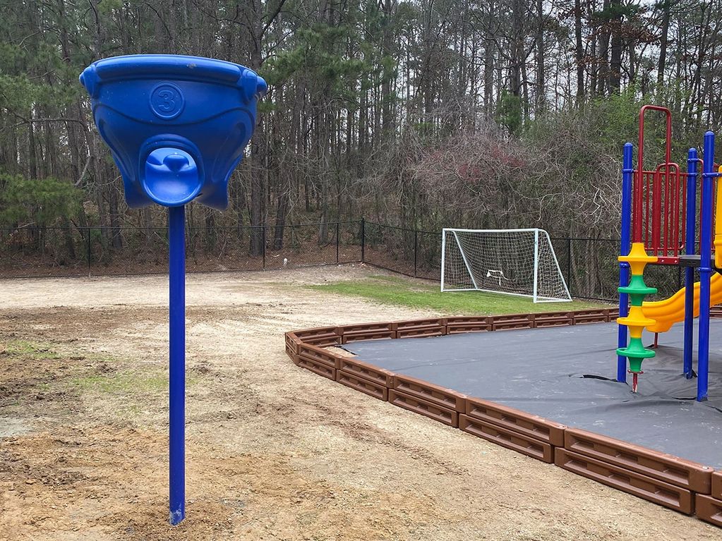 A blue basketball hoop pole near a playground and soccer goal in a park.
