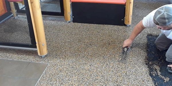 Person applying epoxy resin on a pebble floor surface inside a room.