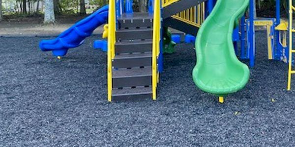 Colorful playground slides and stairs on a rubber mulch surface.