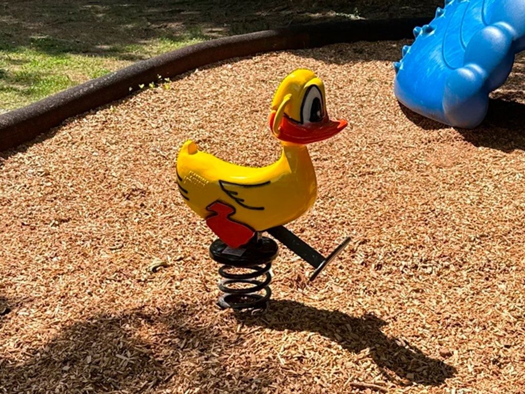 Yellow duck spring rider on playground wood chips.